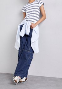Camiseta de manga corta a rayas en azul claro y blanco, combinada con pantalones cargo de mezclilla oscuros y holgados, y zapatillas beige. Camiseta azul claro atada a la cintura.