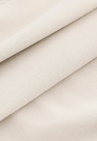Tissu beige clair avec une texture lisse et douce, présentant un tissage simple et un éclat subtil, plié pour révéler de la profondeur et des couches.