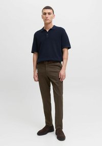 Polo navy de manga corta, chinos marrones y zapatos de lona oscuros. El modelo está de pie contra un fondo blanco liso.