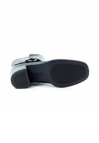 Suela de goma negra de un zapato con textura estriada. Presenta un upper gris con un acabado suave y un detalle decorativo de hebilla plateada.