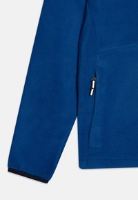 Niebieska polarowa kurtka o miękkiej fakturze. Posiada kieszeń na zamek błyskawiczny i kontrastowy czarny brzeg przy mankietach. Bezszwowy design.