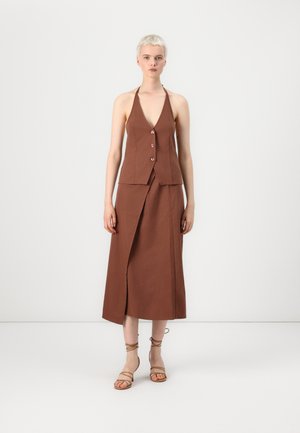 Top marrón con cuello halter y escote en V, adornado con botones en la parte delantera, acompañado de una falda envolvente a juego con una abertura lateral y tiras de tobillo minimalistas.