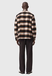 Camicia a scozzese marrone e nera con vestibilità comoda, chiusura a bottoni frontale e maniche lunghe, realizzata in tessuto morbido. I pantaloni sono di un marrone scuro.
