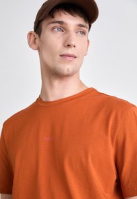 Oransje bomull T-skjorte med rund hals som har en liten rosa "BOSS" logo på brystet. Glatt tekstur, korte ermer.
