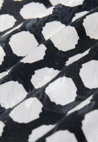 Tessuto in bianco e nero con motivo ottagonale e una texture tattile. La base è prevalentemente nera con forme bianche a contrasto.