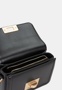 Borsa a tracolla in pelle nera con chiusura in tono oro, compartimenti con zip e texture liscia. L'interno presenta un design foderato.