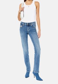 Blå denimjeans med rak passform, hög midja, framfickor och subtila sömdetaljer, kombinerade med en vit ärmlös topp och blå klackskor.