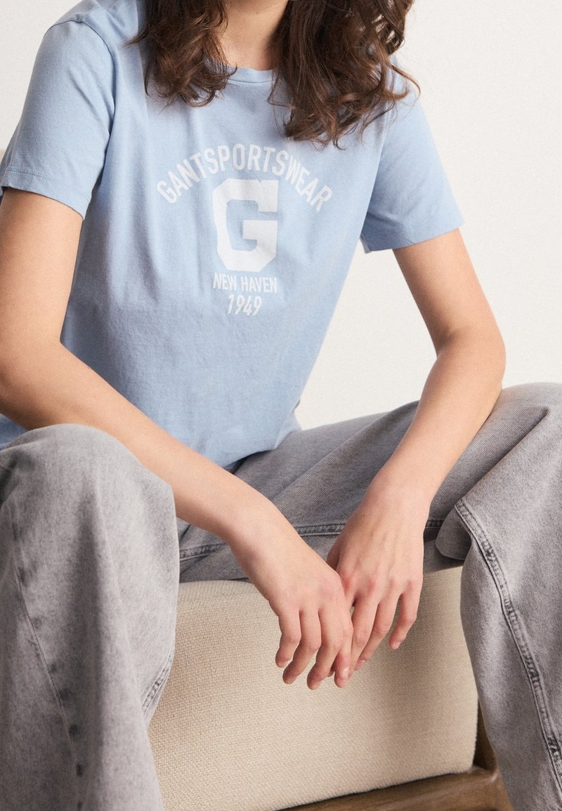 Lichtblauw katoenen T-shirt met het logo "GANT SPORTSWEAR" in het wit, ronde hals, korte mouwen, gecombineerd met grijze brede jeans.