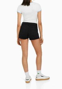 Shorts en jean noir avec ourlet replié, accompagnés d'un haut blanc à manches courtes avec des accents bleu clair. Baskets blanches et chaussettes montantes.