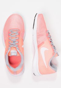 Baskets de course Nike avec une tige en mesh corail respirant, des lacets gris et des accents blancs. Design léger avec une semelle rembourrée.