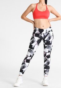 Röd sport-bh i kombination med leggings med svart och vitt geometriskt mönster. Outfiten har en figurnära design och sträckbart tyg för komfort.