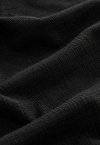 Tissu noir texturé avec un motif en côtes, affichant des plis et des replis, suggérant un matériau doux et léger.
