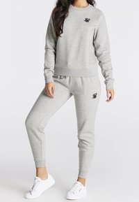 Grijze joggingbroek en sweater set gemaakt van zacht materiaal. Voorzien van een klein zwart logo op de borst en elastische boorden bij de enkels.