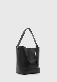 Czarna skórzana torba tote o wyraźnej formie, z kieszenią na zamek błyskawiczny, złotymi detalami oraz pojedynczym paskiem na ramię.