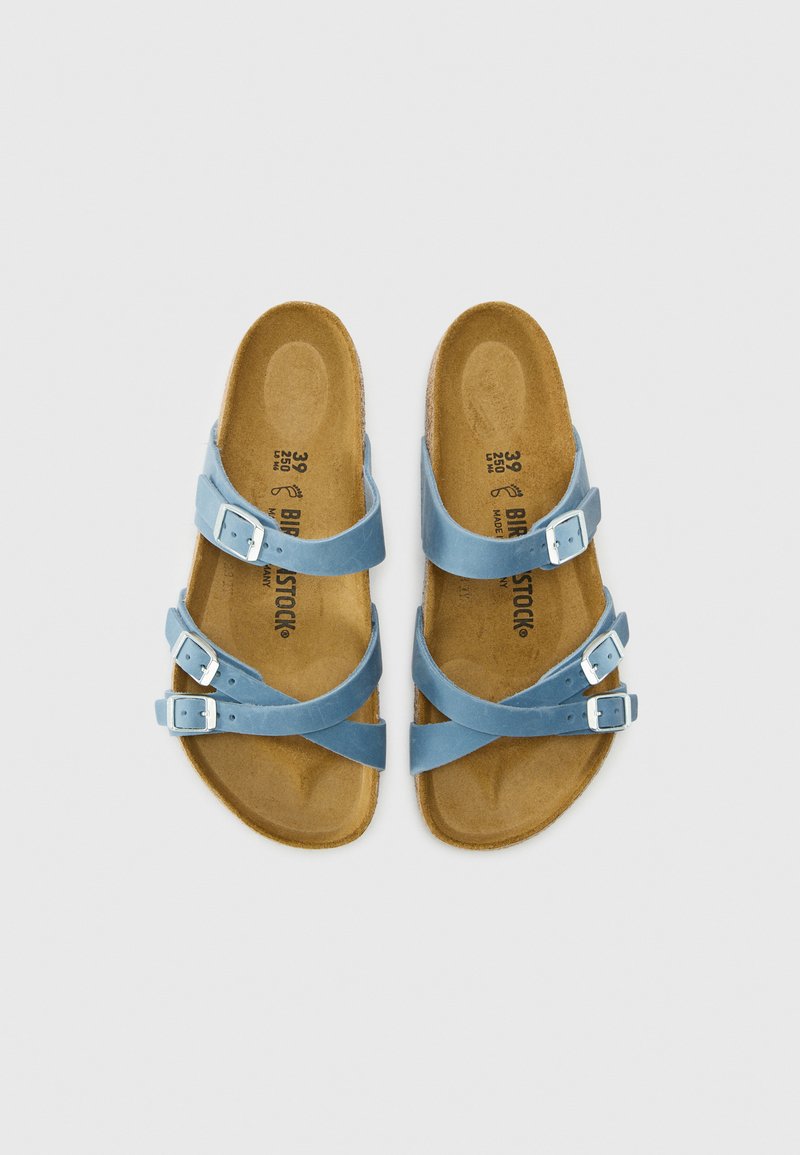 Blauwe Birkenstock-sandalen met drie verstelbare gespsluitingen en gevormde kurken voetbedden, naast elkaar weergegeven op een witte achtergrond.