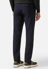 Pantalones marinos de tela elástica, con un ajuste slim, bolsillos traseros, y combinados con zapatillas deportivas en tonos oscuros y claros.