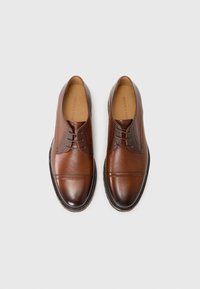 Bruine leren schoenen met een afgeronde neus, subtiele textuur, vetersysteem en contrasterende stiksels langs de rand.