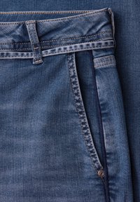 Zbliżenie na niebieskie jeansy z denimu, ukazujące pętlę na pasek, boczną kieszeń z widocznym przeszyciem oraz detal z metalowym nitonkiem.