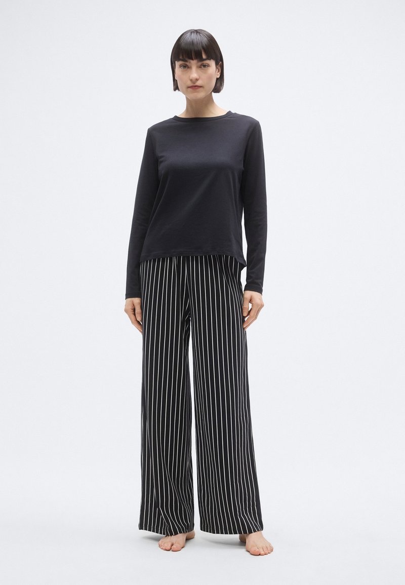 Haut noir à manches longues avec un col rond, associé à un pantalon à jambes larges à rayures noires et blanches. Tissu doux avec une coupe ample.