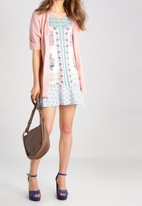 Kukallinen lyhythihainen mekko, jossa valkoinen pohja ja siniset sekä vaaleanpunaiset kuviot, yhdistettynä vaaleanpunaiseen paitaan, ruskeaan käsilaukkuun ja sinisiin korkokenkiin.