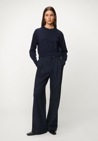 Granatowy dzianinowy sweter z okrągłym dekoltem, zestawiony z granatowymi spodniami o szerokich nogawkach, zapięty na guziki i o gładkiej fakturze, uzupełniony czarnymi butami.