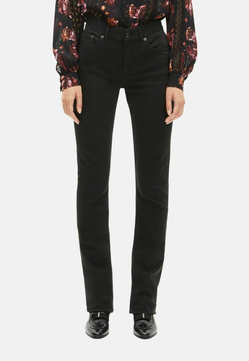 Jeans negros slim fit con una textura suave, diseño de cinco bolsillos y detalles de costura sutiles. Combinados con un top de flores de manga larga.
