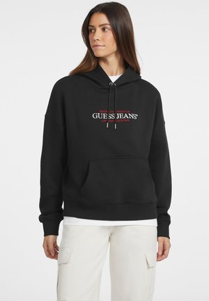 Crna dukserica od pamuka s prednjim džepom, kapuljačom s vezicom i izvezenim "GUESS JEANS" logotipom u crvenoj i bijeloj boji.