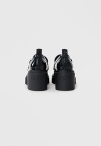 Μαύρα παπούτσια πλατφόρμας με γυαλιστερή φινίρισμα, με παχύ πέλμα και ανάγλυφο λογότυπο στη φτέρνα. Λουριά με λεπτομέρειες λογότυπου στο πίσω μέρος.