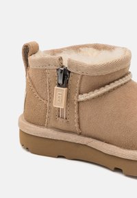 Tan suede ankle boot with a fur lining, featuring a side zipper, stitched accents, and a rubber sole.