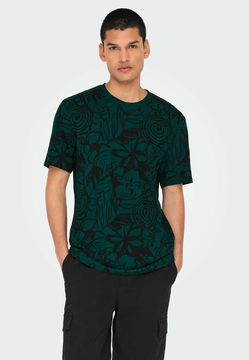 Camiseta de color verde oscuro con un patrón floral negro, escote redondo, mangas cortas y un corte relajado, hecha de una tela suave.