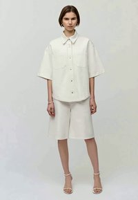 White denim short-sleeve shirt with two chest pockets, paired with matching knee-length shorts. Smooth fabric, relaxed fit, and minimal design.