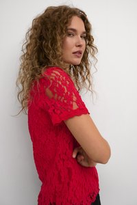 Top en dentelle rouge à manches courtes, présentant un motif floral, des bords festonnés et une silhouette ajustée. Texture lisse avec des éléments transparents.