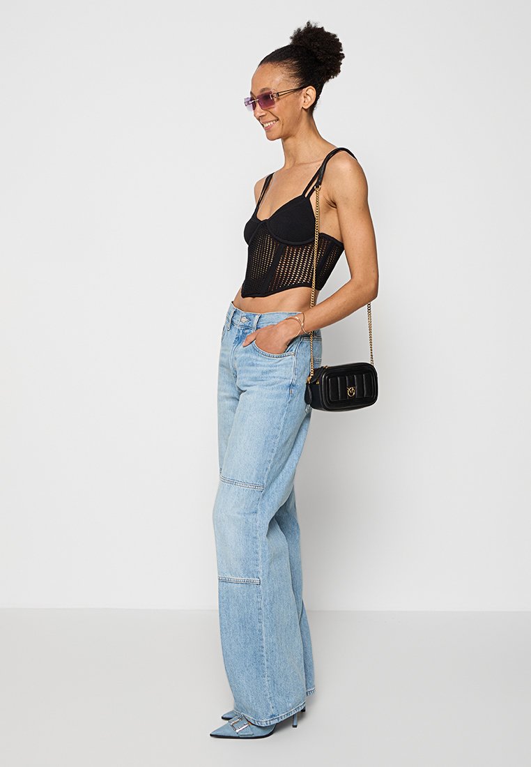 Schwarzes Mesh-Crop-Top mit verstellbaren Trägern, kombiniert mit hellblauen weiten Jeans. Als Accessoires ein kleiner schwarzer Handtasche mit Kettenriemen.