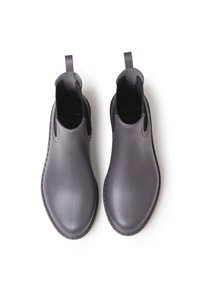 Botas de tobillo de goma negra con textura suave, paneles elásticos laterales y pestañas de agarre para facilitar su uso. Suela plana negra con bordes cosidos.