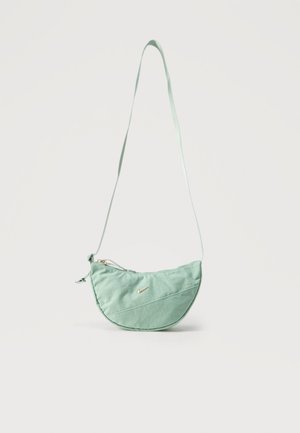 Halvemaanvormige crossbodytas in muntgroen met lange riem, diagonale naad, ritssluiting en een klein gouden Nike-swooshlogo aan de voorkant.