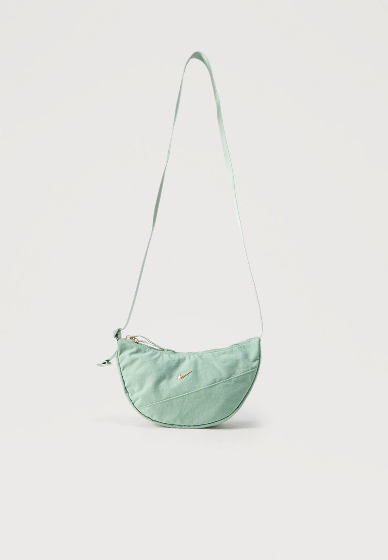 Mintno zelena torbica za čez ramo v obliki polmeseca z dolgim paščkom, diagonalnim šivom, zadrgo in majhnim zlatim Nike logotipom v obliki kljuna spredaj.