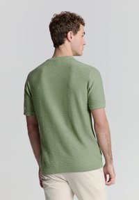 Lichtgroene gebreide trui met korte mouwen en een ronde halslijn, met een gladde textuur en ribgebreide zoom. De achterkant toont een getailleerd ontwerp.