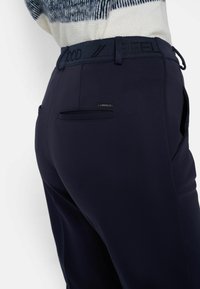Pantaloni navy con una texture liscia e una cintura elastica con la stampa "FEEL GOOD". Comprendono tasche posteriori e sottili dettagli metallici.