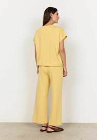 Gelbes Set bestehend aus einem entspannten Kurzarm-Top und weiten Hosen. Glatte Textur, lässiges Design und minimale Details.