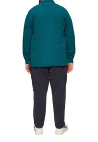 Tealfarbener Langarmpullover mit Kragen, kombiniert mit dunkelblauen Hosen. Leichter Stoff, lockere Passform und minimale Nahtdetails.