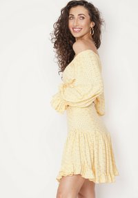 Żółta sukienka bez ramiączek z bufiastymi rękawami, falbaniastym dołem, fakturowanym materiałem oraz haftowanymi wzorami na całej powierzchni.