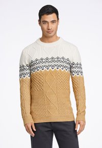 Stickad tröja med en krämfärgad övre del och svarta geometriska mönster samt en gyllenbrun nedre del med texturerade diamantmönster.