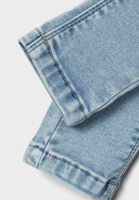Jeans de mezclilla azul claro con un acabado desgastado. Las características incluyen costuras dobles en los puños y una textura suave.