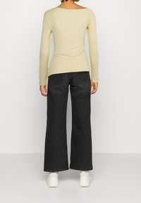 Pitkähiha, vaalean beige paita, jossa on leveä kaula-aukko ja kontrastoiva neonkeltaiset ompeleet. Yhdistetty korkeavyötäröisten, leveälahkeisten tummansinisien farkkujen kanssa.