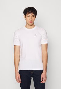 Camiseta blanca de algodón con cuello redondo y mangas cortas; presenta un pequeño logo negro en el lado izquierdo del pecho; corte casual.