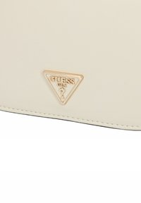 Portafoglio color crema con una finitura testurizzata e un logo oro triangolare impresso nell'angolo in basso a sinistra. Presenta cuciture bianche lungo il bordo.