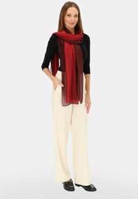 Czerwona i bordowa szal w gradient, noszony na czarnej bluzce, zestawiony z kremowymi spodniami o szerokich nogawkach i czarnymi mokasynami. Gładka faktura, elegancko układa się.