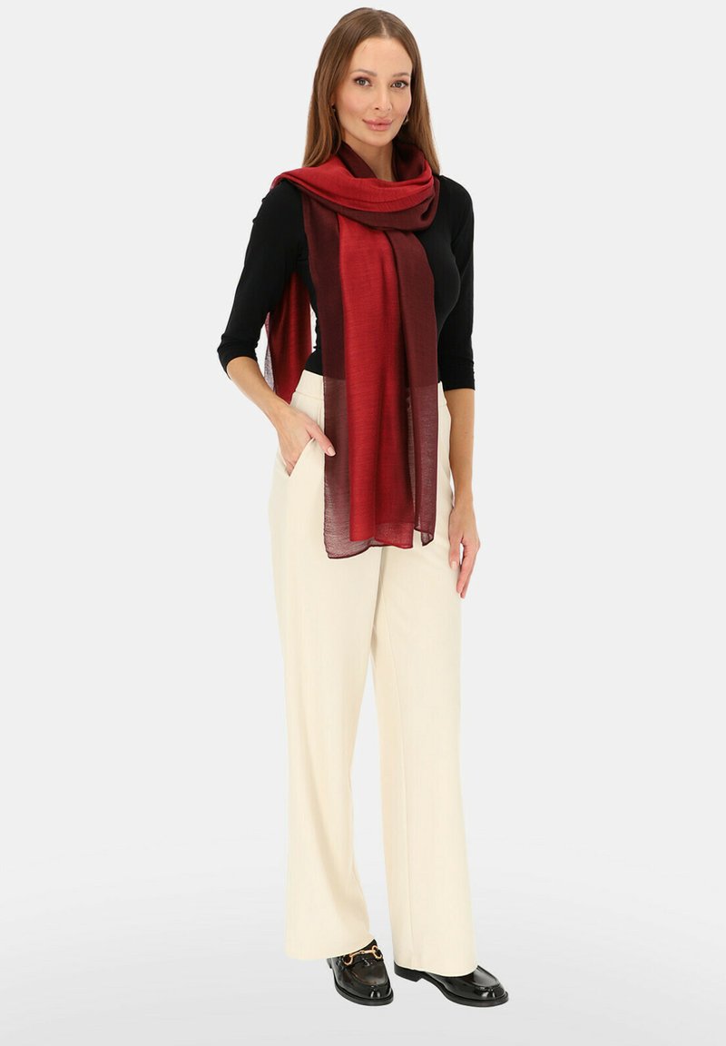 Czerwona i bordowa szal w gradient, noszony na czarnej bluzce, zestawiony z kremowymi spodniami o szerokich nogawkach i czarnymi mokasynami. Gładka faktura, elegancko układa się.