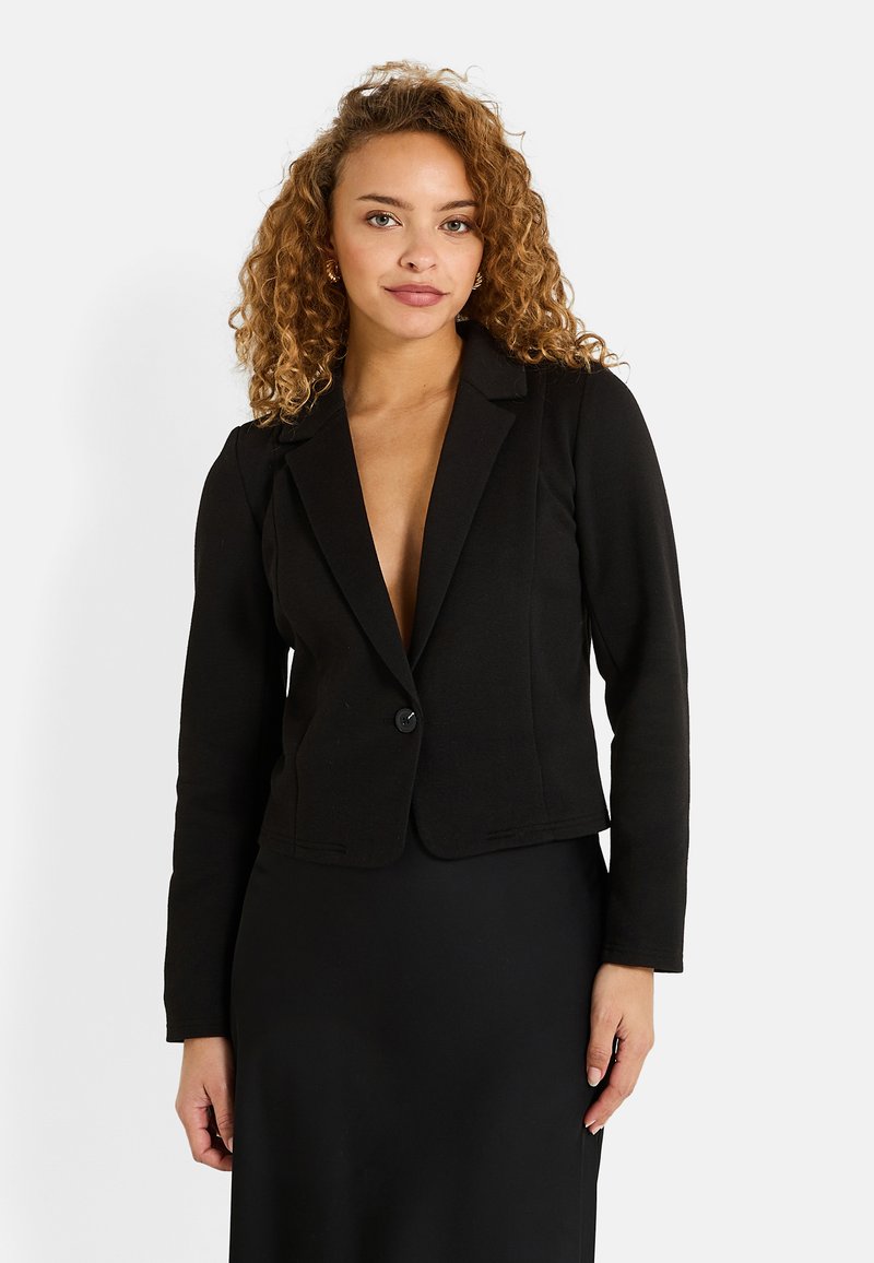 Blazer ajustado negro con cierre de un solo botón, solapas con muesca y mangas largas. Textura suave, diseñado para una silueta entallada.