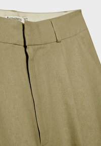Pantalon beige taille haute avec passants pour ceinture, fermeture à boutons dissimulée sur le devant et tissu doux texturé.
